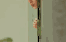 a young man is peeking out of a doorway .