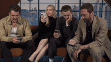 a group of people sit on a couch looking at their phones