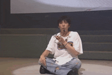 a man wearing a white shirt that says rea on it sits on the floor