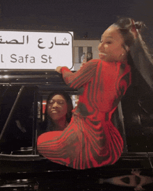 a woman in a red dress stands in front of a sign that says safa st.