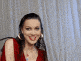 a woman wearing a red sweater , necklace , and hoop earrings is smiling .