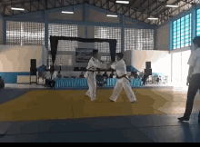 a man in a white belt is fighting another man in a red belt in a gym