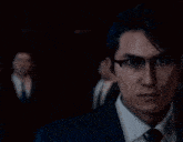 a man in a suit and tie with glasses is looking at the camera