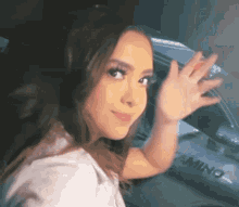 a woman is standing in front of a car and waving at the camera .