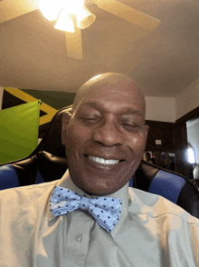 a man wearing a bow tie is smiling in front of a green and yellow flag
