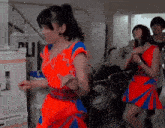 a woman in a red and blue dress is dancing in a room with a sign that says ' ali ' on it