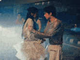 a woman in a white dress is hugging a man in silver