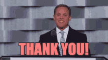 a man in a suit and tie is standing at a podium and saying thank you !