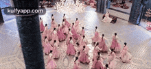 a group of women in pink dresses are dancing in a room with a chandelier .