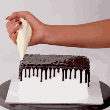 a person is frosting a cake with white frosting and chocolate drips