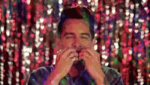 a man with a beard is covering his mouth with his hands in front of a curtain with hearts on it .