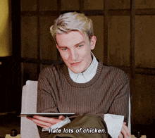 a young man in a brown sweater is holding a tablet and saying late lots of chicken