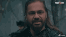 a man with long hair and a beard is standing in front of a trt hd logo .