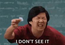 a man is holding a piece of paper in front of a blackboard and saying `` i do n't see it '' .