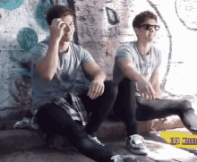two men are sitting next to each other in front of a wall with graffiti on it and a yellow sign that says los melli