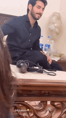 a man in a black shirt is sitting on a table next to a bottle of aquafina water