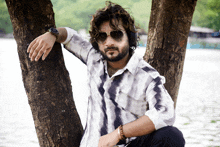 a man leaning against a tree wearing sunglasses