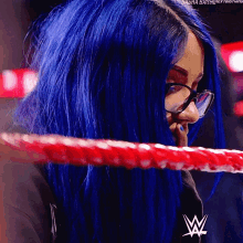 a woman with blue hair is wearing glasses and has a w logo on her shirt