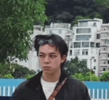 a young man wearing sunglasses and a shoulder bag is standing in front of a building .