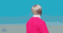 a young man wearing a pink shirt with a white letter s on the front is standing in front of a blue sky ..
