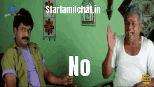 two men are sitting at a table and one of them has the word no on his chest