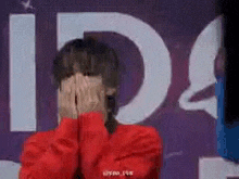 a woman in a red sweater is covering her face with her hands in front of a sign .