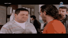 a man in an orange shirt is talking to another man in a gray shirt
