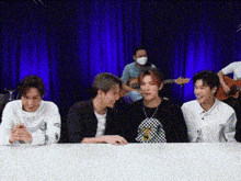 a group of young men are sitting at a table in front of a blue curtain and laughing .