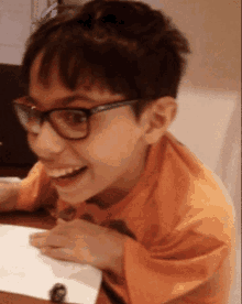 a young boy wearing glasses and an orange shirt is sitting at a table
