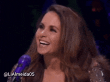 a woman singing into a purple microphone with the name lialmeida05 on the bottom right