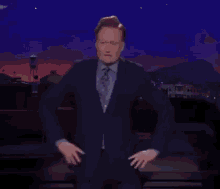 a man in a suit and tie is standing with his hands on his hips on a stage at night .