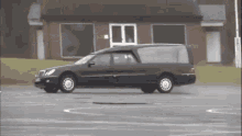 a black funeral car is driving in a parking lot in front of a building .