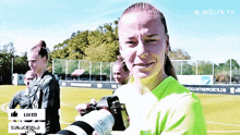 a woman in a green shirt is holding a camera with the word liked below it