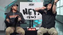 two men are sitting in front of an aew sign