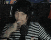a man wearing headphones and a striped shirt is talking into a microphone with his eyes closed