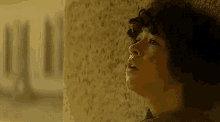 a young boy with curly hair leaning against a wall with his mouth open