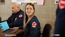 a man and a woman are sitting at a table with a laptop and a sign that says #chicagofire