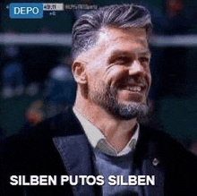 a man with a beard is smiling and wearing a suit and sweater .