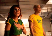 a man wearing a yellow shirt with a brazilian flag on it stands next to a woman wearing a green shirt