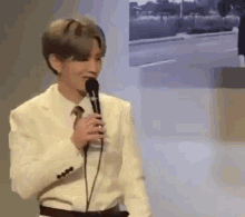 a man in a white suit and tie is holding a microphone and singing into it .