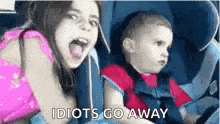 a little girl and a little boy are sitting in a car seat and making funny faces .