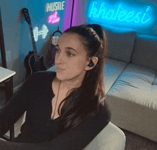 a woman wearing headphones sits in front of a neon sign that says hustle