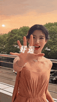 a woman in a pink dress holds up her hand in front of a sunset