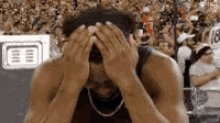 a man is covering his face with his hands while sitting in a stadium .