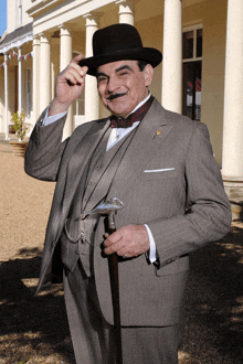 a man in a suit holds a cane and adjusts his hat