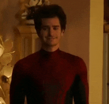 a man in a red spiderman costume is standing in a room and smiling .