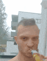 a man with a mohawk drinking from a bottle with a building in the background