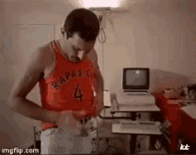 a man wearing a red tank top with the number 4 on it is standing in front of a computer .