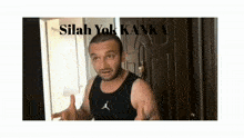 a man in a black tank top is standing in front of a door with the words silah yok kanka above him .
