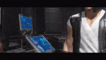 a man in a white shirt and black vest is standing in front of a computer screen .